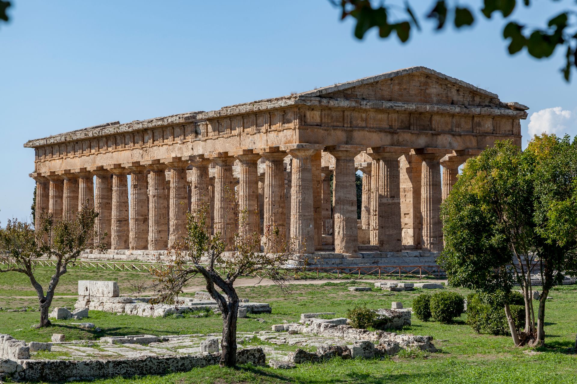 Il cosiddetto tempio di Nettuno a Paestum, tempio dorico con colonne in pietra chiara, circondato da prato e alberi sotto un cielo azzurro